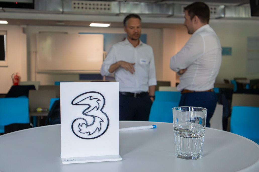 Im Vodergrund das Logo von DREI. Und im Hintergrund unscharf Clemens Nachgebauer und noch eine Person